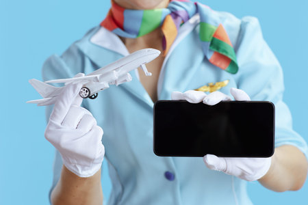 Closeup on female air hostess against blue background in blue uniform with a little airplane showing...