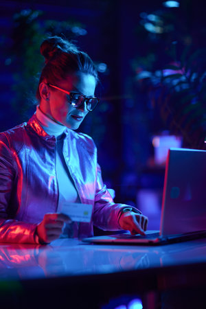 Neon metaverse futuristic concept. trendy business woman in glasses with credit card using laptop in modern office.の写真素材