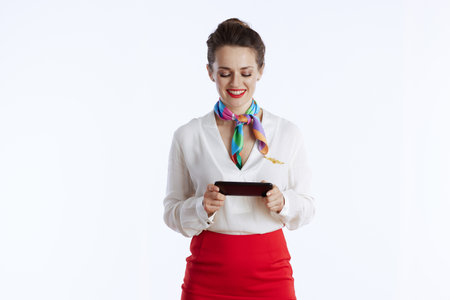smiling modern female stewardess against white background in uniform using smartphone applications.の写真素材