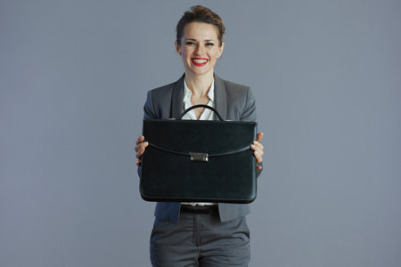 smiling stylish woman worker in gray suit with briefcase isolated on gray background.の写真素材