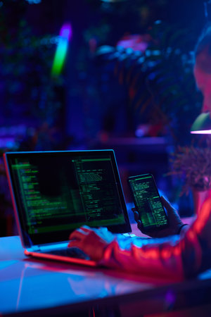 Seen from behind modern woman with laptop and smartphone developing video game.の写真素材