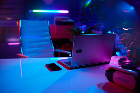 Neon metaverse futuristic concept. modern office with desk, laptop and virtual reality goggles.の写真素材