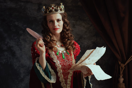 happy medieval queen in red dress with parchment and crown on dark gray background.