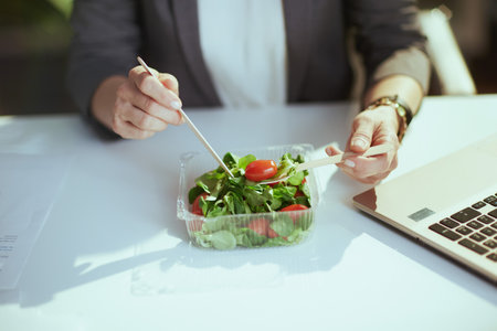 Sustainable workplace. Closeup on woman employee in green office with laptop eating salad.の写真素材