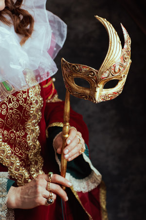 Closeup on medieval queen in red dress with venetian mask and white collar on dark gray background.の写真素材