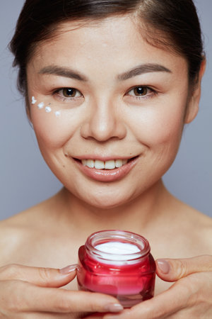 Portrait of young asian female with facial cream jar and facial cream on face on blue background.の写真素材