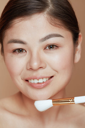 Portrait of modern Asian female with makeup brush against beige background.の写真素材