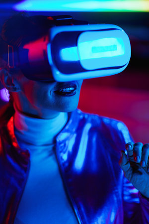 Neon metaverse futuristic concept. happy elegant 40 years old woman in virtual reality goggles in modern office.の写真素材
