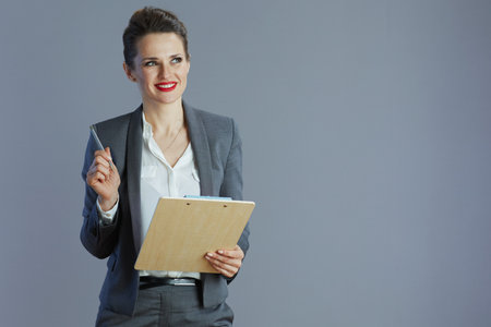 happy modern small business owner woman in gray suit with clipboard isolated on gray background.の写真素材