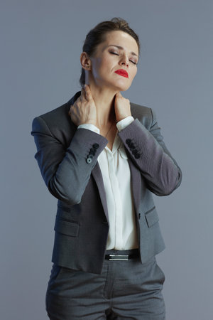 tired young female worker in gray suit having neck pain against gray background.の写真素材