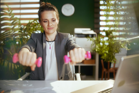 Sustainable workplace. happy modern small business owner woman in modern green office with dumbbells.の写真素材