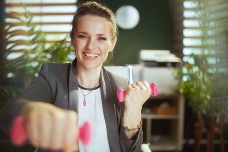 Sustainable workplace. happy modern small business owner woman in modern green office with dumbbells.の写真素材
