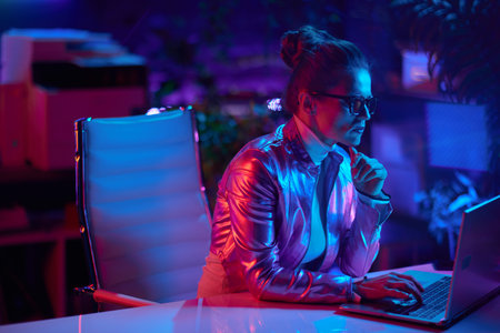 Neon metaverse futuristic concept. pensive elegant woman in glasses with laptop in modern office.