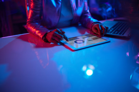 Neon metaverse futuristic concept. Closeup on middle aged woman with tablet PC and laptop working with charts in office.の写真素材