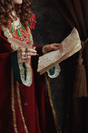 Closeup on medieval queen in red dress with parchment on dark gray background.の写真素材