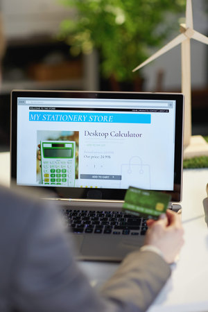 Seen from behind modern female with laptop and credit card browsing online shop in modern office.