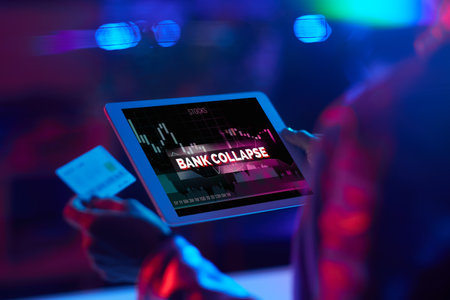 Seen from behind modern business woman with credit card using tablet PC with bank collapse screenの写真素材