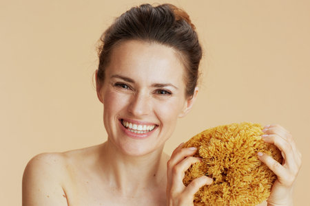 smiling modern woman with sea sponge against beige background.の写真素材