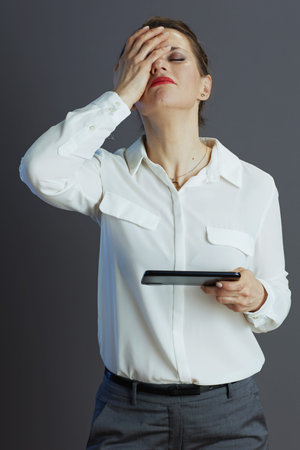 stressed trendy woman worker in white blouse with smartphone against gray background.