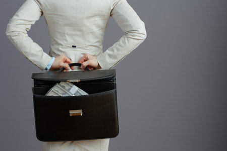 Seen from behind female worker in a light business suit with briefcase and dollar money packs isolated on grey.の写真素材