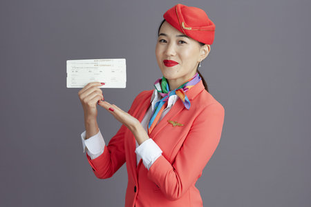 happy elegant stewardess asian woman in red skirt, jacket and hat uniform with flight tickets...