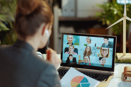 Seen from behind modern business woman with laptop having video call in modern office.