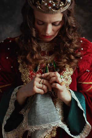 unhappy medieval queen in red dress with handkerchief and crown on dark gray background.の写真素材