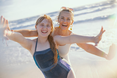 Portrait of smiling modern mother and teenage daughter at the beach in beachwear having fun time.の写真素材