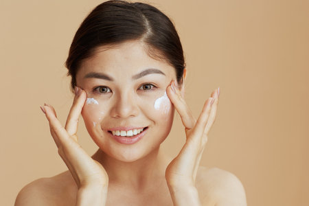 Portrait of modern woman with facial cream on face on beige background.の写真素材