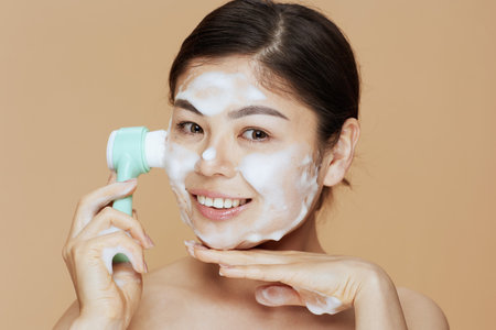 Portrait of young asian woman with massager washing face on beige background.の写真素材