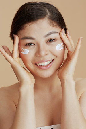 Portrait of modern asian female with facial cream on face isolated on beige background.の写真素材