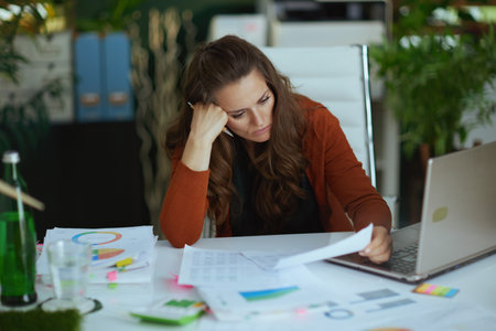 tired elegant small business owner woman with laptop working with documents in the modern green office.の写真素材