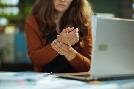 Closeup on small business owner woman with laptop and wrist pain in the green office.の写真素材