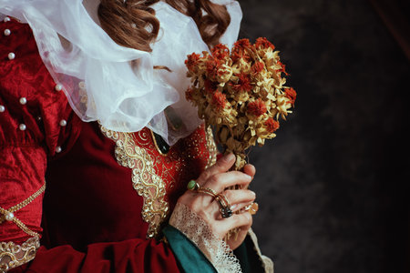 Closeup on medieval queen in red dress with dried flower and white collar on dark gray background.の写真素材