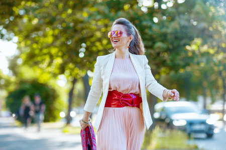 smiling modern woman in pink dress and white jacket in the city with sunglasses walking.の写真素材