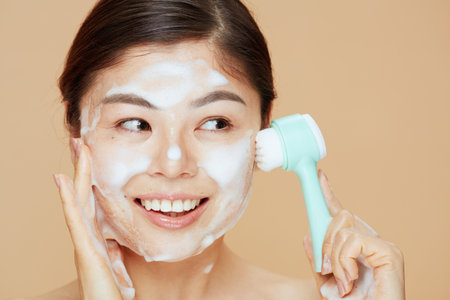 young woman with massager washing face on beige background.の写真素材