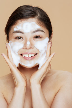 Portrait of young asian woman washing face isolated on beige background.の写真素材