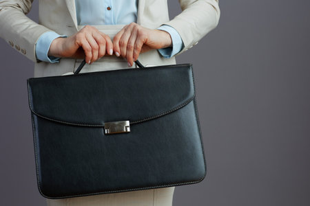 Closeup on female worker in a light business suit with briefcase against gray background.の写真素材