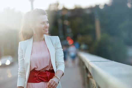 happy trendy 40 years old woman in pink dress and white jacket in the city on the bridge.の写真素材