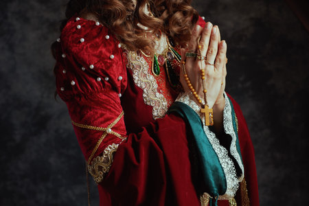 Closeup on medieval queen in red dress with rosary praying on dark gray background.の写真素材