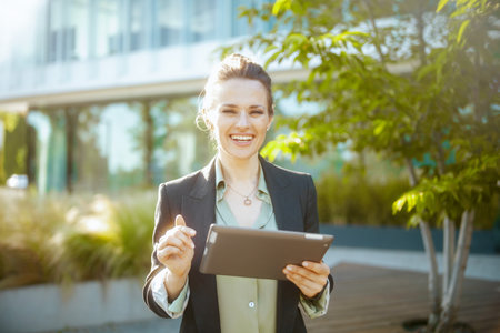 smiling modern 40 years old woman employee near business center in black jacket with tablet PC.の写真素材