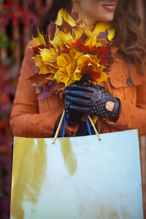 Hello September. happy trendy female in orange trench coat with shopping bags and autumn yellow leaves in the city.の写真素材