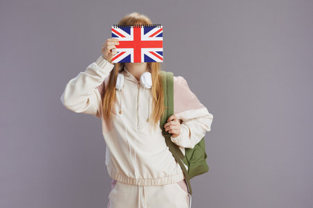 modern teen girl in beige tracksuit with backpack, english flag workbook and headphones isolated on gray background.の写真素材