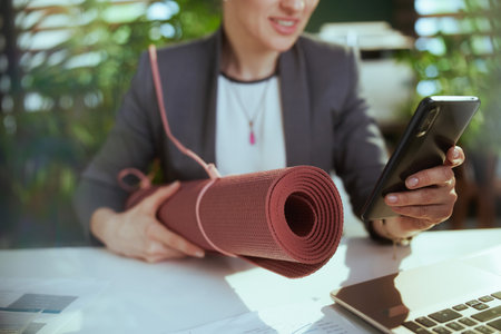 Sustainable workplace. Closeup on modern small business owner woman at work with yoga mat and smartphone.の写真素材