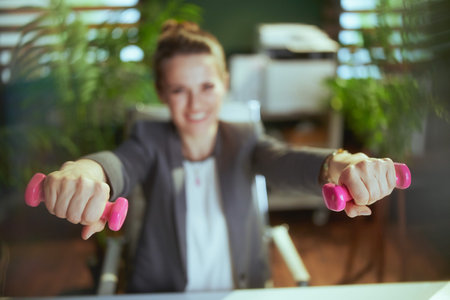 Sustainable workplace. Closeup on happy modern small business owner woman at work with dumbbells.の写真素材