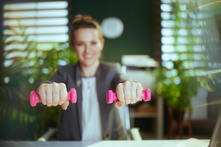Sustainable workplace. Closeup on smiling modern business woman at work with dumbbells.の写真素材