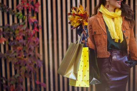 Hello September. smiling young female in orange trench coat with shopping bags and autumn yellow leaves in the city.の写真素材