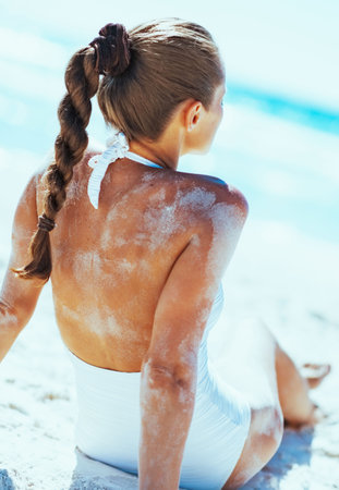 Young woman in swimsuit sitting on sandy beach and sunbathingの写真素材