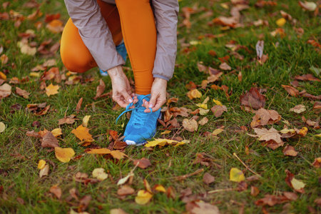 Hello autumn. Closeup on woman in fitness clothes in the park tying shoelaces.の写真素材