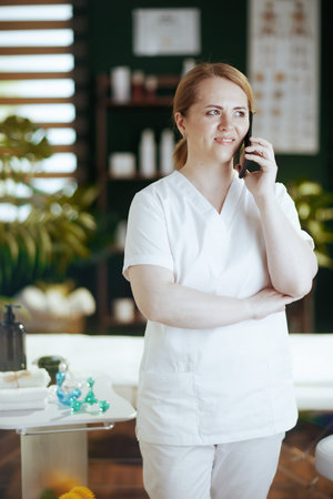 Healthcare time. happy female massage therapist in spa salon talking on a smartphone.の写真素材